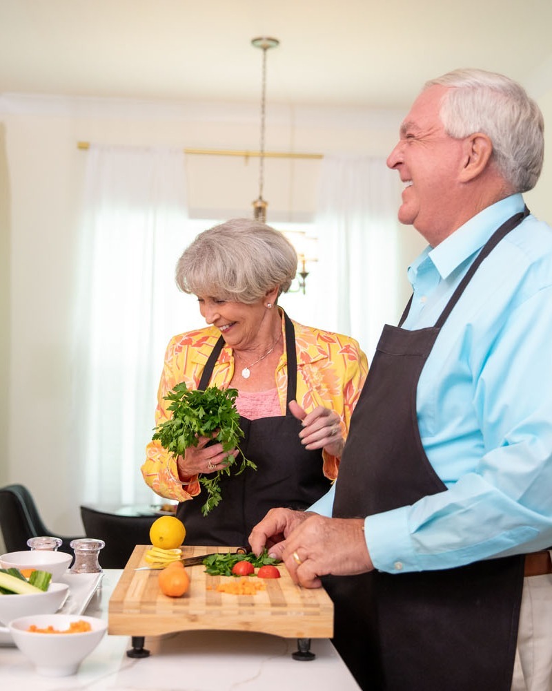 A smiling couple prepares fresh vegetables together at a kitchen island, reflecting the engaging senior lifestyle near Sandy Springs, GA and Buckhead, GA.