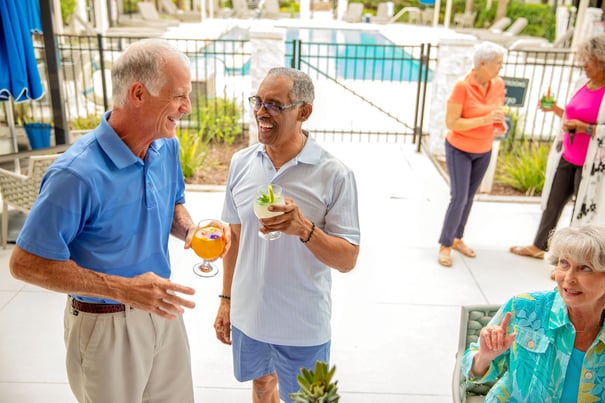 A group of older adults laughs and mingles over refreshing drinks on a sunny outdoor patio, enjoying the vibrant social lifestyle available at a senior living community in Athens, GA.