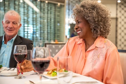 Two older adults enjoy glasses of red wine and a meal together at an elegantly set dining table, reflecting the warm, social on-site dining experience at senior living in Fort Myers, FL.