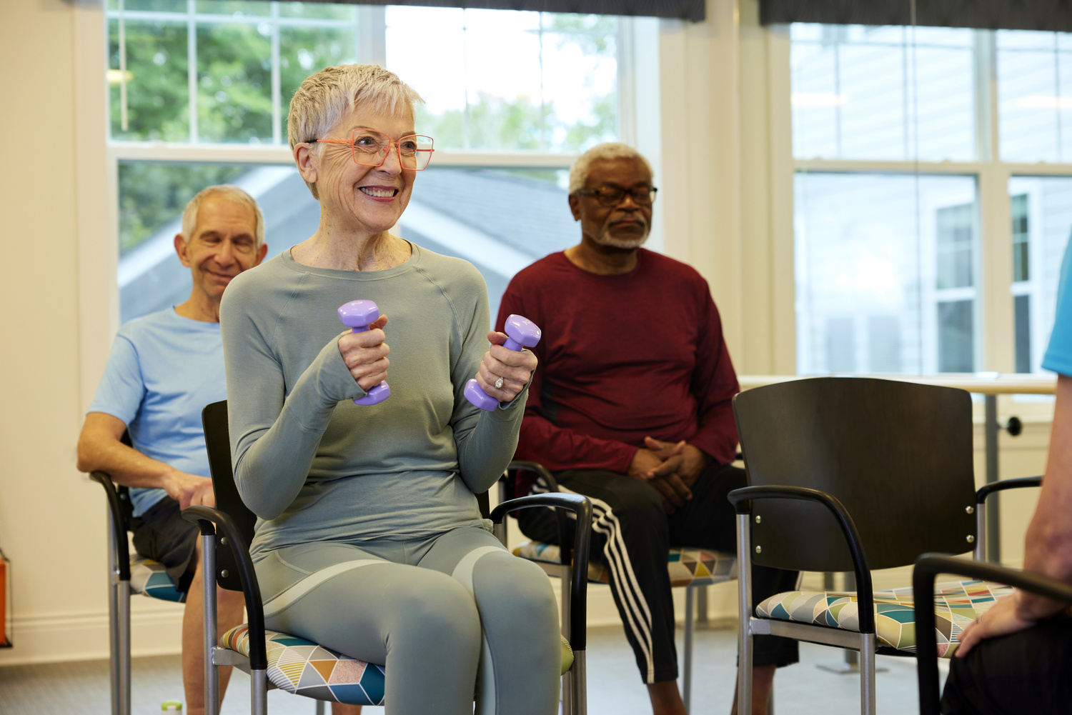 A group of residents lifts light dumbbells together during a fitness class, showcasing the engaging senior lifestyle programs near Sandy Springs, GA and Perimeter, GA.