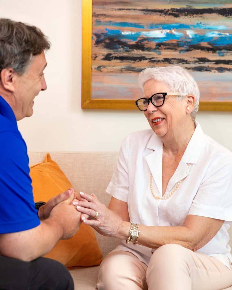 A man and woman share a warm moment holding hands together beside a colorful abstract painting, reflecting the caring senior living in Sandy Springs, GA and Dunwoody, GA.