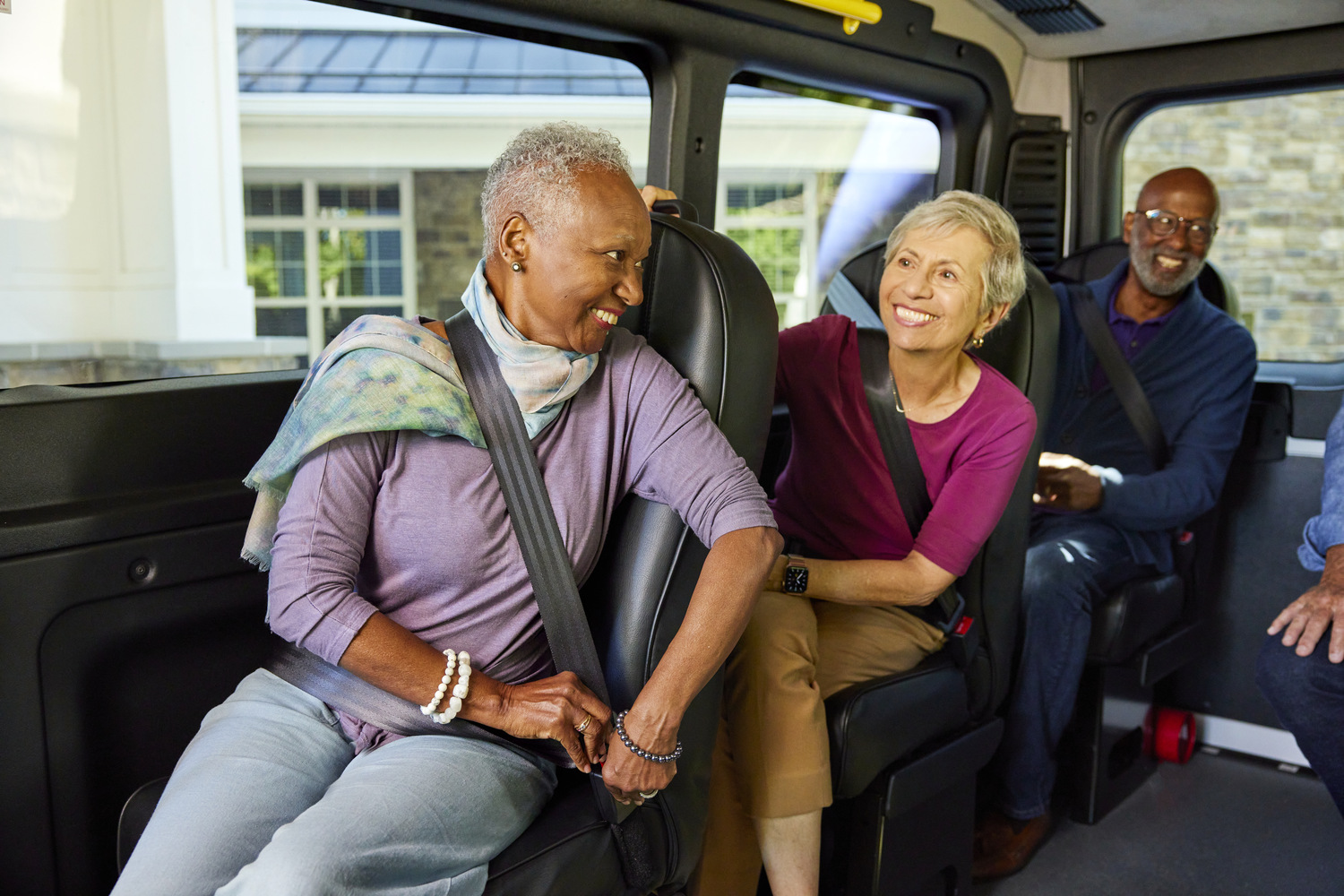 Three residents smile together while seated and buckled in a community shuttle van, reflecting the convenient senior living in Sandy Springs, GA and North Atlanta, GA.