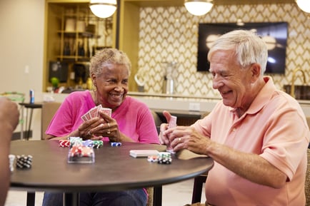 Two residents share a lively card game with poker chips at a community game table, capturing the vibrant social atmosphere and active senior living lifestyle in Decatur, GA.