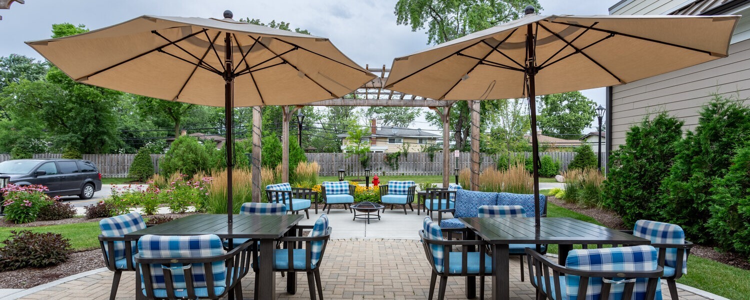 The outdoor patio at Arbor Terrace Glenview senior living features umbrella covered tables for dining and relaxing, ideal for North Shore senior living with outdoor amenities.