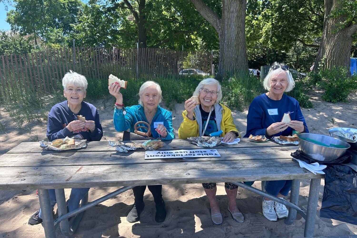 Community members smile and enjoy a sunny picnic lunch together outdoors, capturing the active senior lifestyle Glenview residents experience at this senior living community.