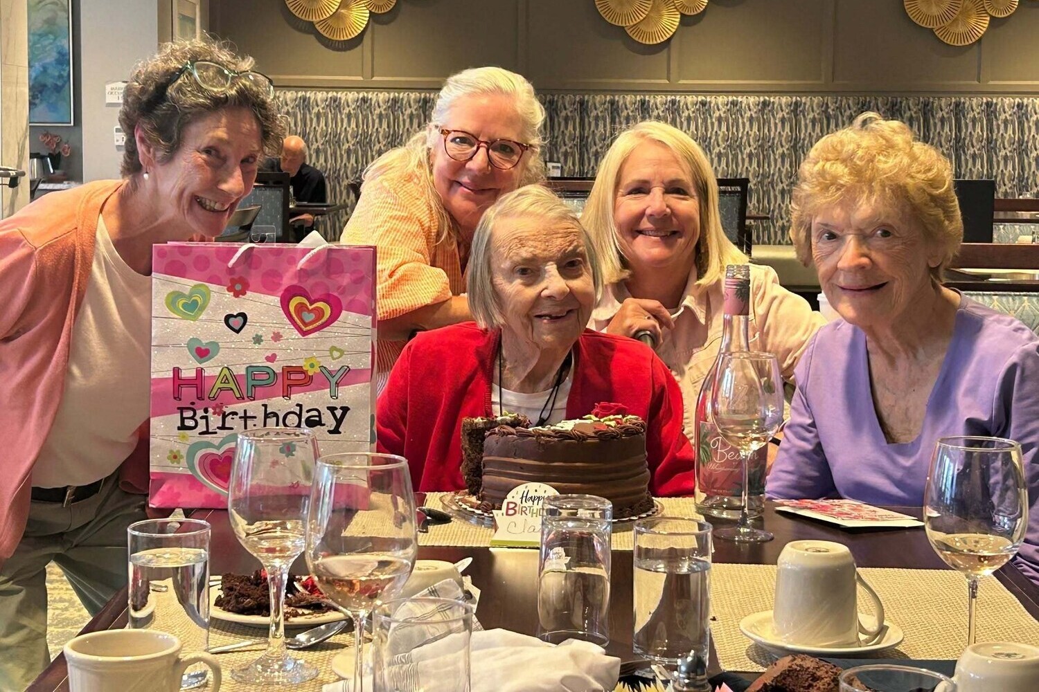 A group of five community members gathers around a chocolate cake to celebrate a birthday together, reflecting the active senior lifestyle Glenview residents enjoy at this Glenview senior living community.
