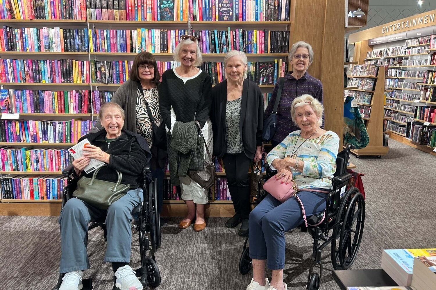 A cheerful group of community members gather among the bookshelves at a local bookstore outing, part of the active senior lifestyle Glenview residents enjoy at this senior living community.