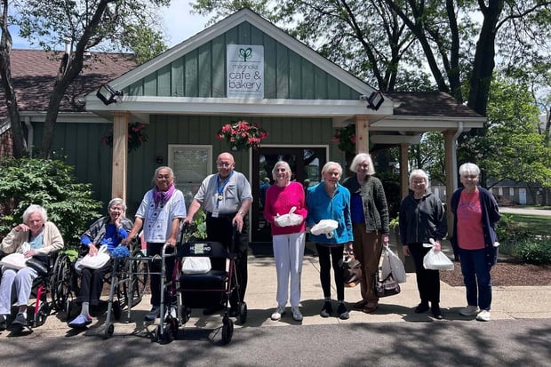A cheerful group of community members poses together outside a local cafe during a community outing, reflecting the active senior lifestyle Glenview residents enjoy through the senior care Glenview Illinois provides.