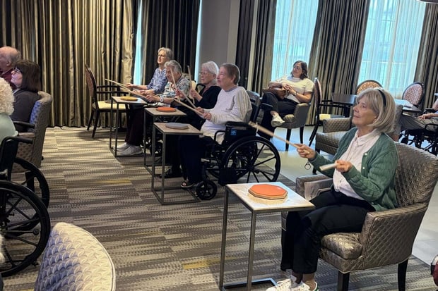 A group of community members takes part in a lively group exercise activity together in a bright common area, part of the senior living with wellness programs Glenview IL offers at this Glenview senior living community.