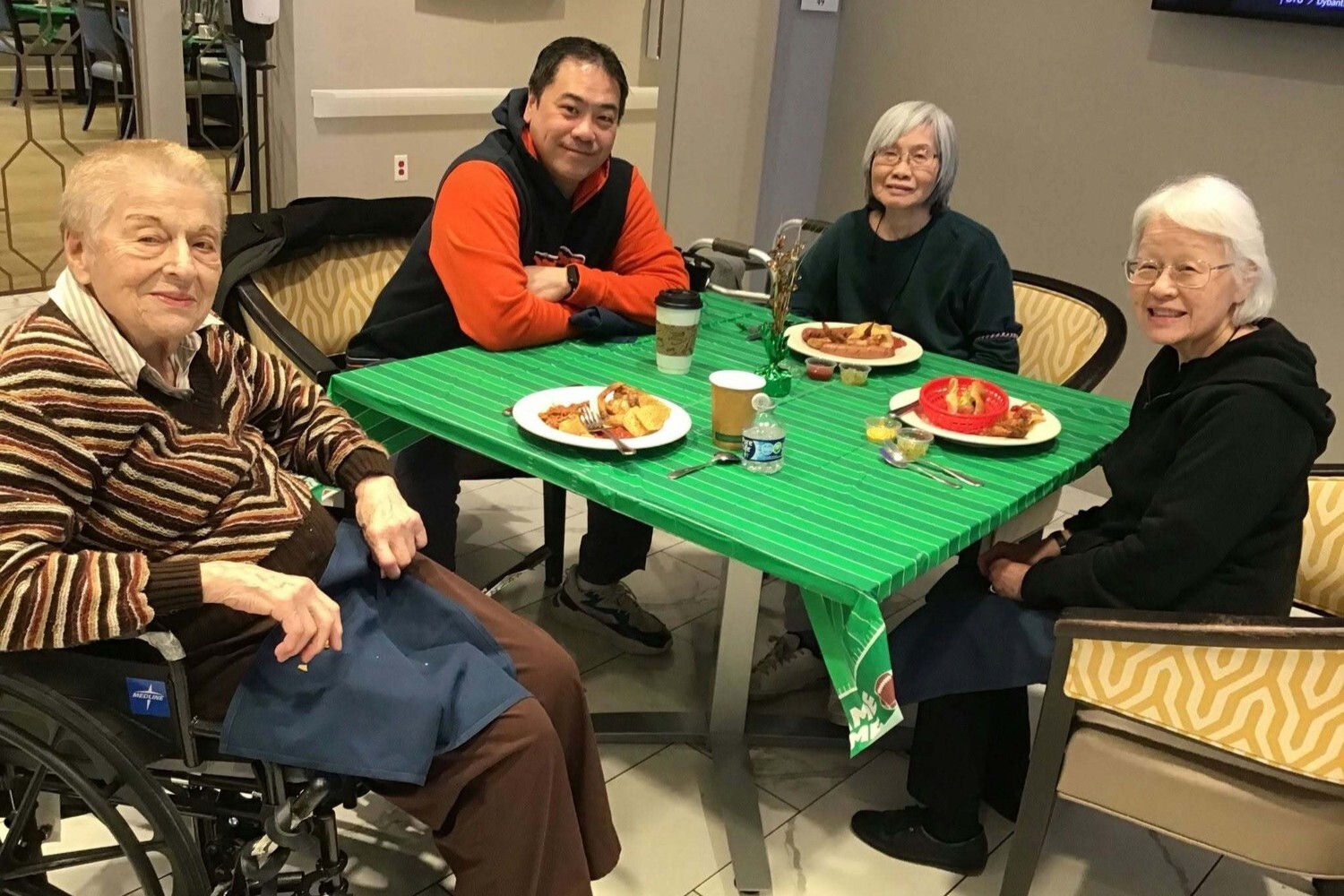 A group of four community members gathers for a game day meal together at a festively decorated table, reflecting the active senior lifestyle Glenview residents enjoy at this Glenview senior living community.