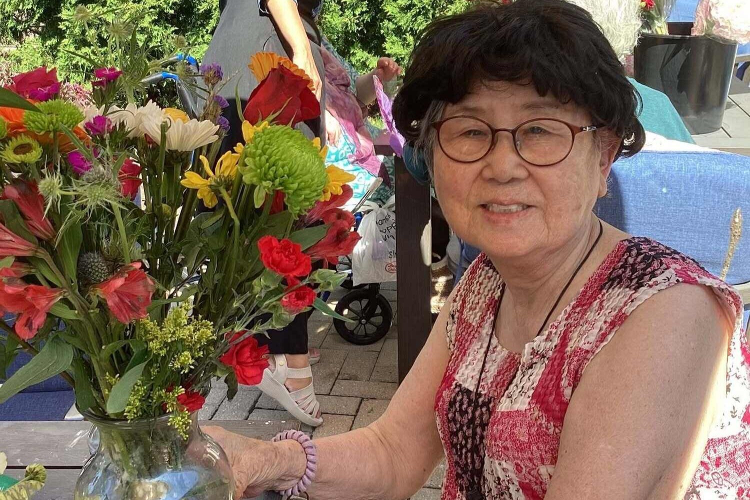 A smiling community member sits beside a vibrant bouquet of fresh flowers outdoors, part of the senior care Glenview Illinois this Glenview senior living community with parks and walking paths provides.