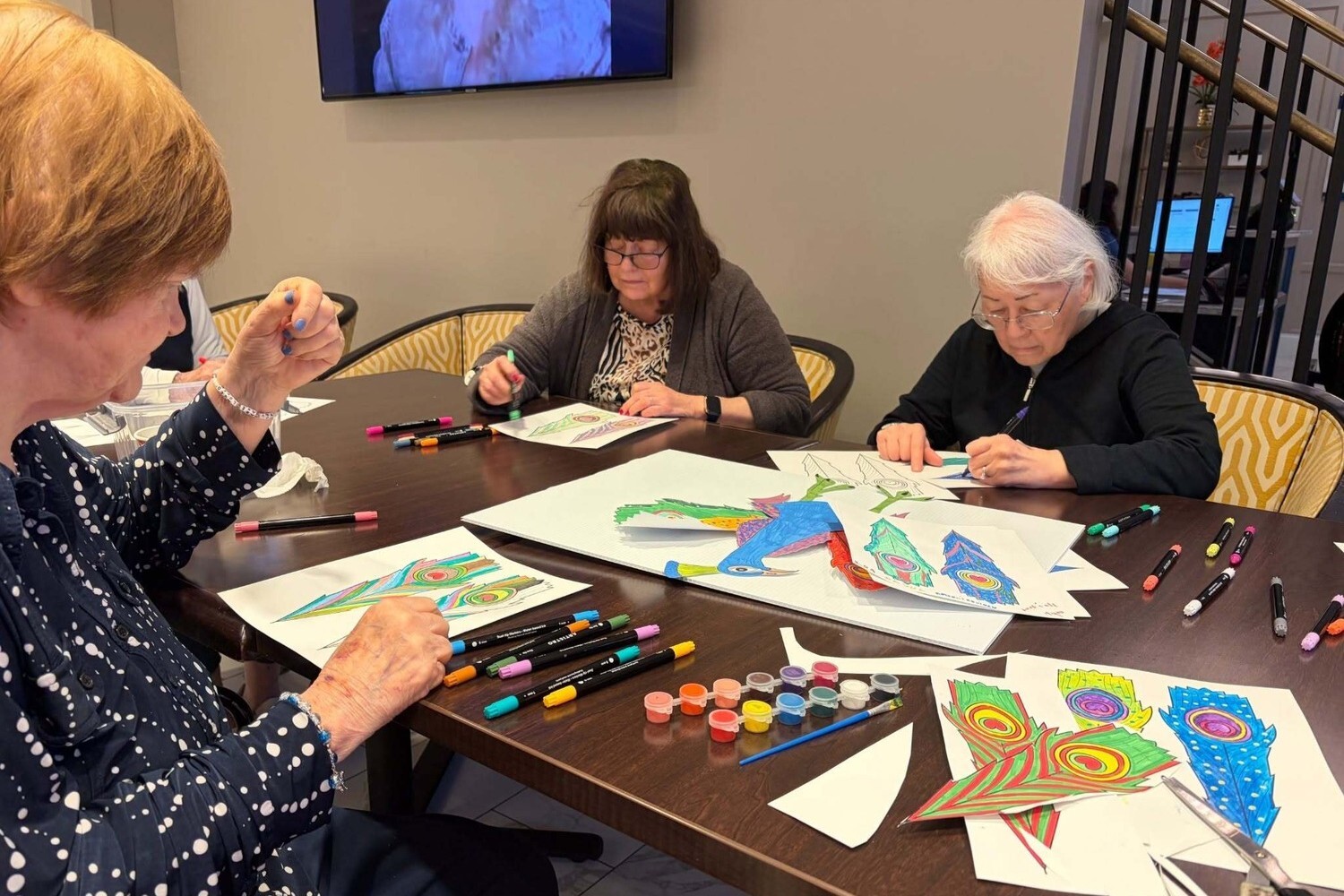A group of community members color detailed peacock feather designs together at a table, part of the senior living with wellness programs Glenview IL offers at this top-rated senior living Glenview community.
