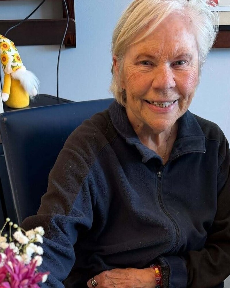A smiling community member sits beside a bouquet of fresh pink flowers at this top-rated senior living Glenview community, reflecting the warmth found at this Glenview senior living community.
