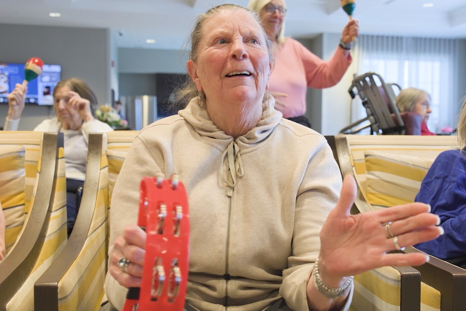 A resident at Arbor Terrace Glenview senior living joyfully shakes a rhythm instrument during a lively music session, part of the active senior lifestyle Glenview offers.