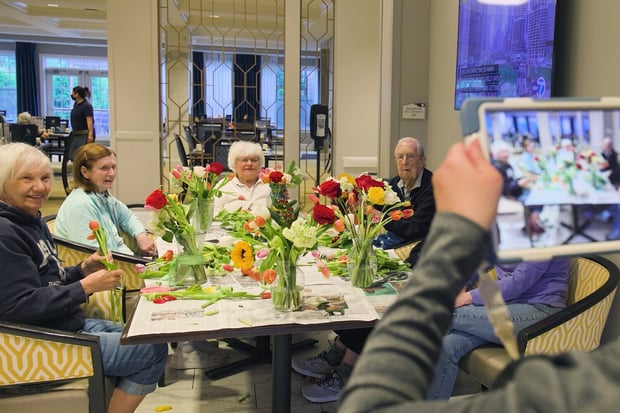 Residents at Arbor Terrace Glenview senior living gather around a table filled with fresh flowers during a group activity, embracing the active senior lifestyle Glenview IL provides.