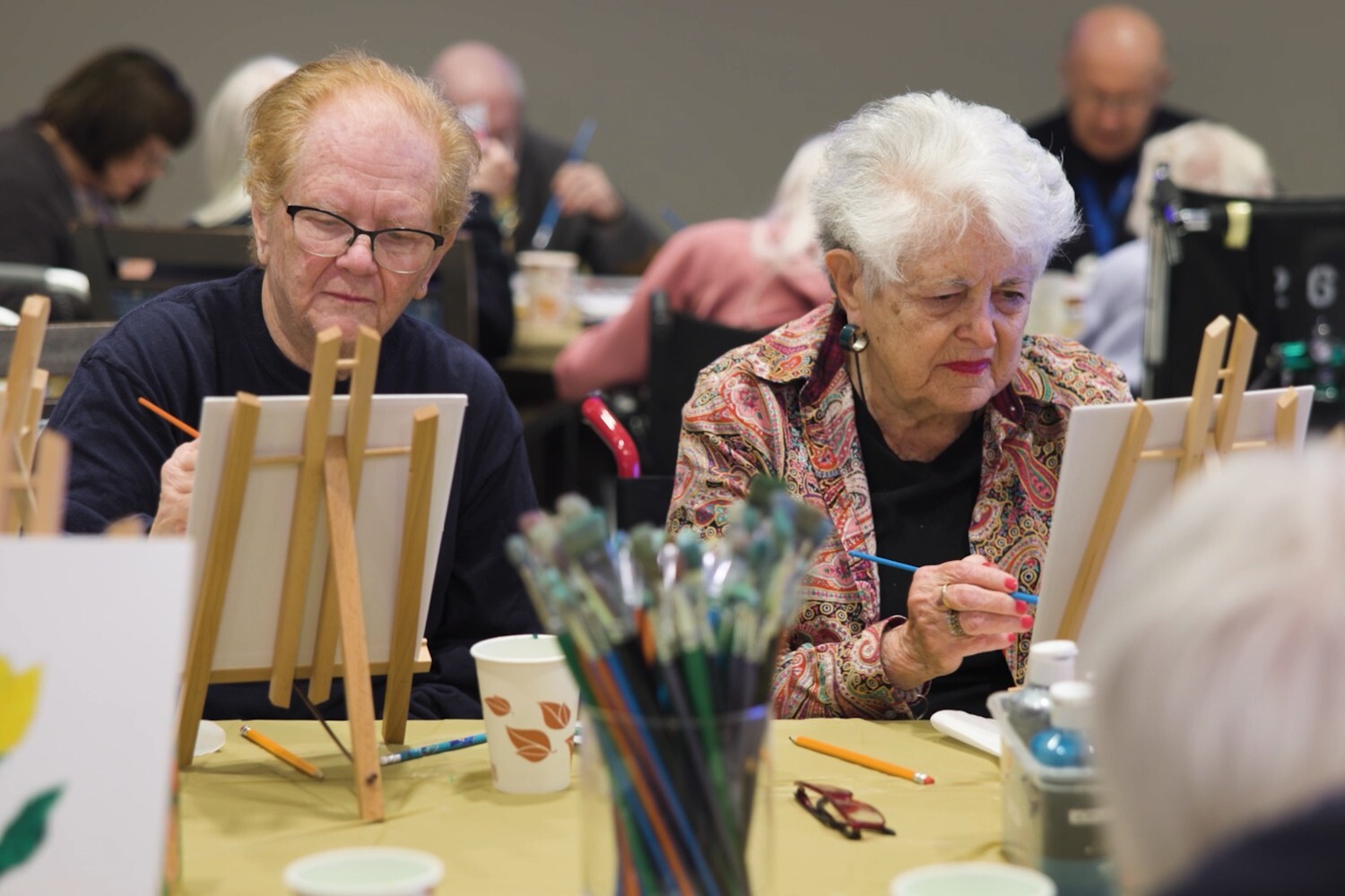 Residents at Arbor Terrace Glenview senior living paint together at easels during a group art class, embracing the creative, active senior lifestyle Glenview offers.