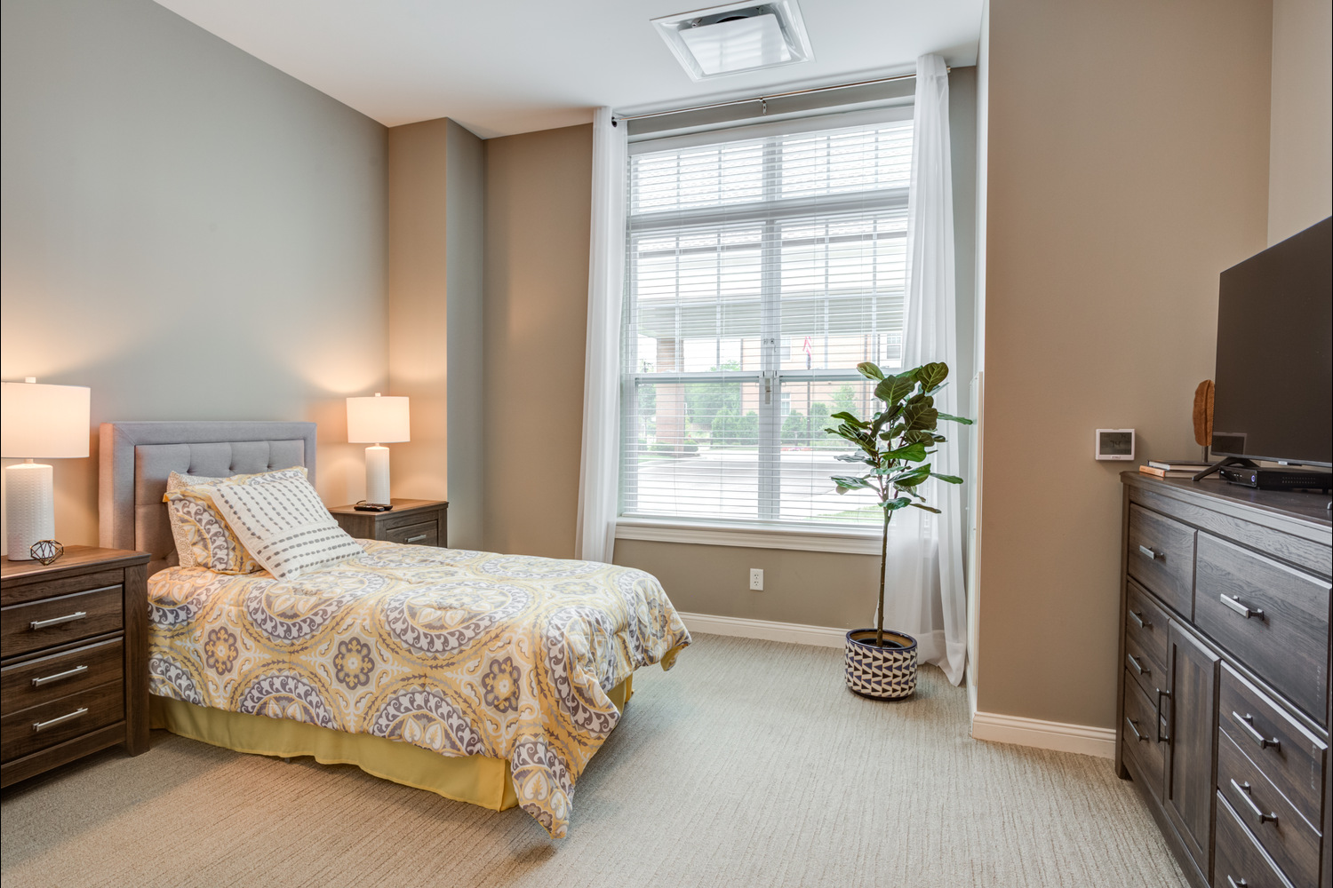 The bedroom at Arbor Terrace Glenview senior living features a comfortable bed, television, and bright natural light, part of the assisted living in Glenview Illinois lifestyle.