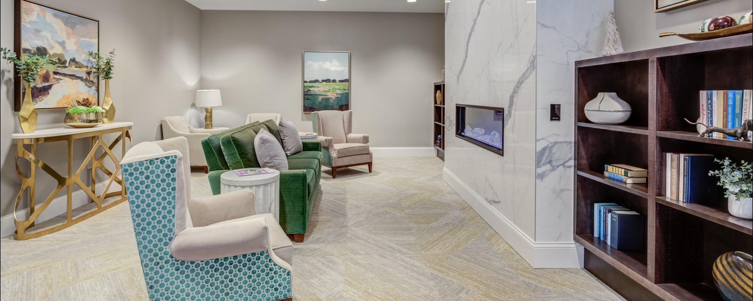 A bright, inviting living room lounge with a marble fireplace, built-in bookshelf, and cozy teal and green seating at this top-rated senior living Glenview community, part of the active senior lifestyle Glenview offers.