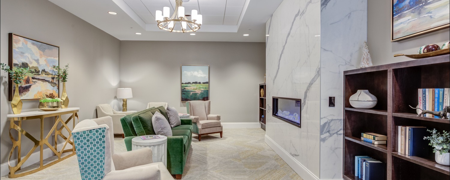 A bright, inviting living room lounge with a marble fireplace, built-in bookshelf, and cozy teal and green seating at this top-rated senior living Glenview community, part of the active senior lifestyle Glenview offers.