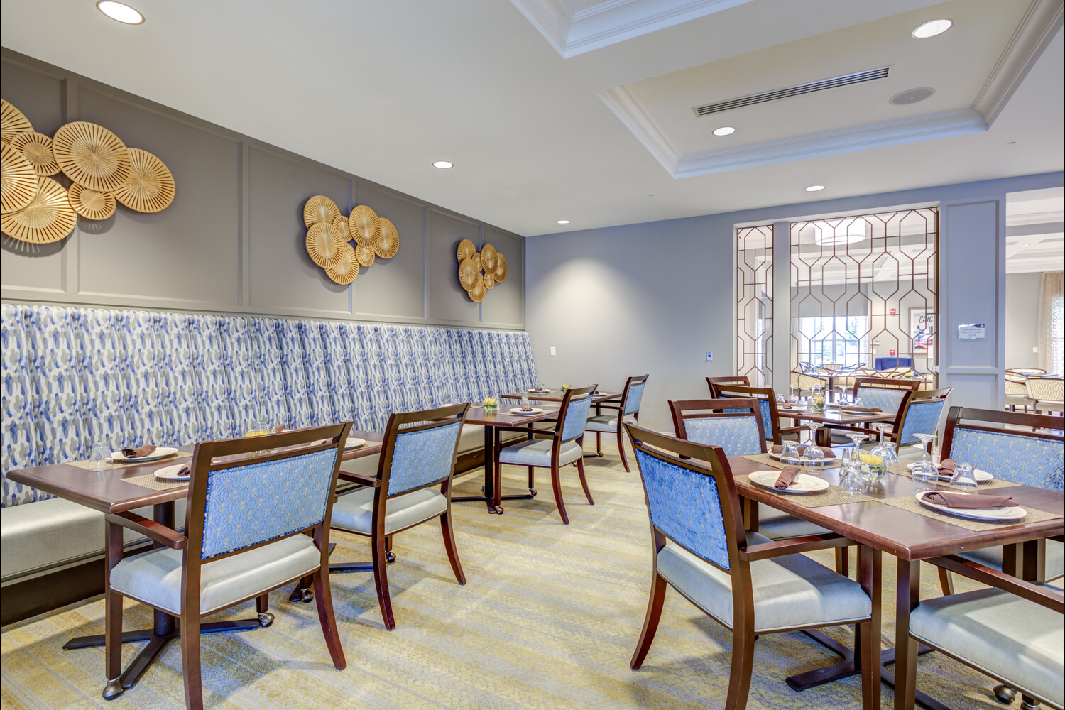The dining room at Arbor Terrace Glenview senior living showcases blue upholstered chairs and decorative wall art, reflecting senior living with gourmet dining North Shore.