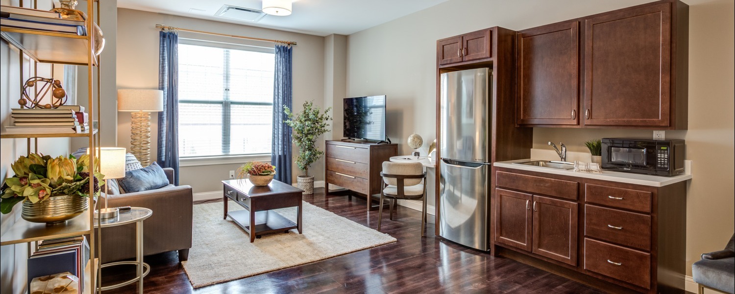 A well-appointed apartment kitchen and living area with rich wood cabinetry, stainless steel appliances, and cozy furnishings at this Glenview senior living community, part of the best senior living in Chicago's North Shore suburbs.