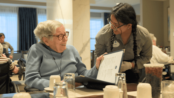 A resident smiles while reviewing a menu with a caring staff member, reflecting the personalized senior living found in Glenview, IL communities.