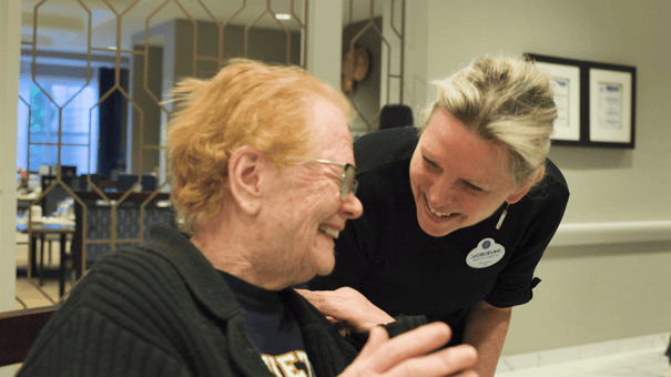 A team member shares a warm, joyful laugh with a resident in the elegant lobby at Arbor Terrace Glenview, reflecting the wellness programs and Glenview senior living experience found at this community.