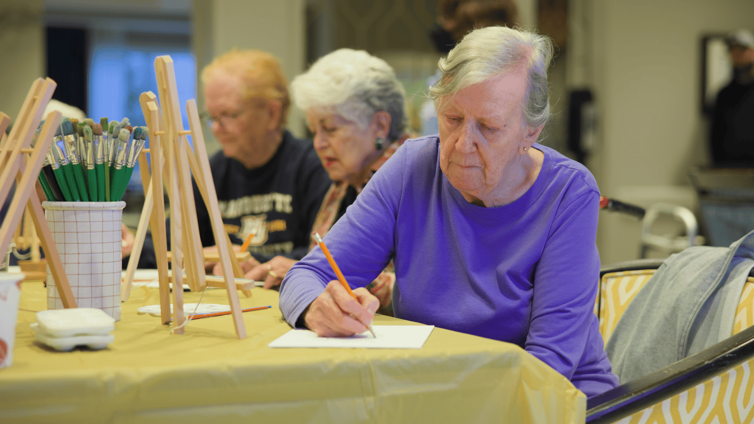 A resident at Arbor Terrace Glenview senior living focuses intently while painting during a creative art class, enjoying the active senior lifestyle Glenview offers.