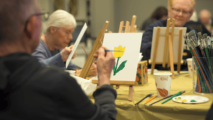A resident carefully paints a yellow tulip during an art class, showcasing senior living with wellness programs and senior care with activities in Glenview.