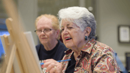 A resident at Arbor Terrace Glenview senior living paints alongside a companion during a creative art class, embracing the active senior lifestyle Glenview offers.
