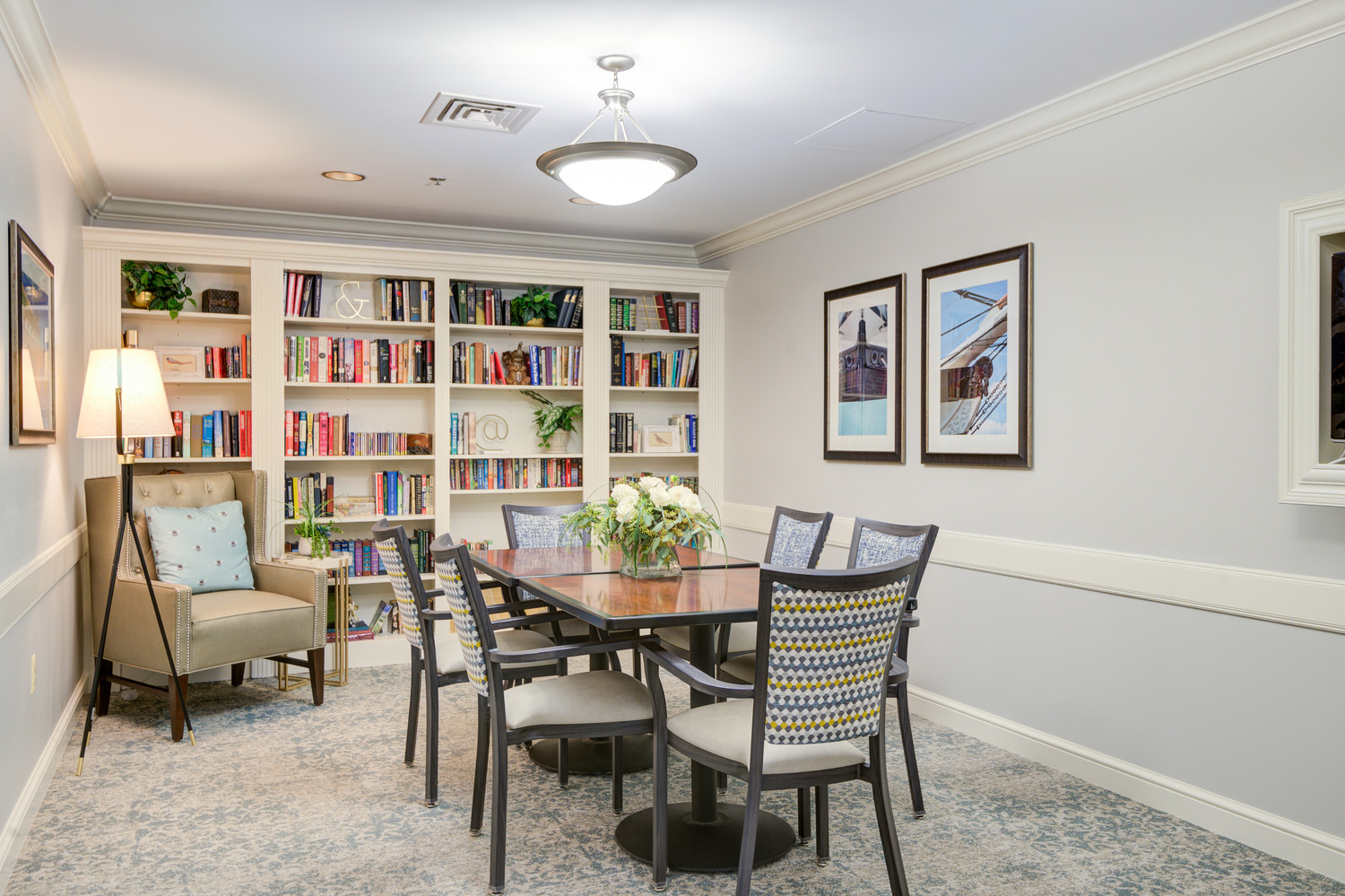 Bright dining room with wood tables, patterned chairs, and built-in bookshelves at Arbor Terrace, offering senior living with on-site dining in Lanham, MD.
