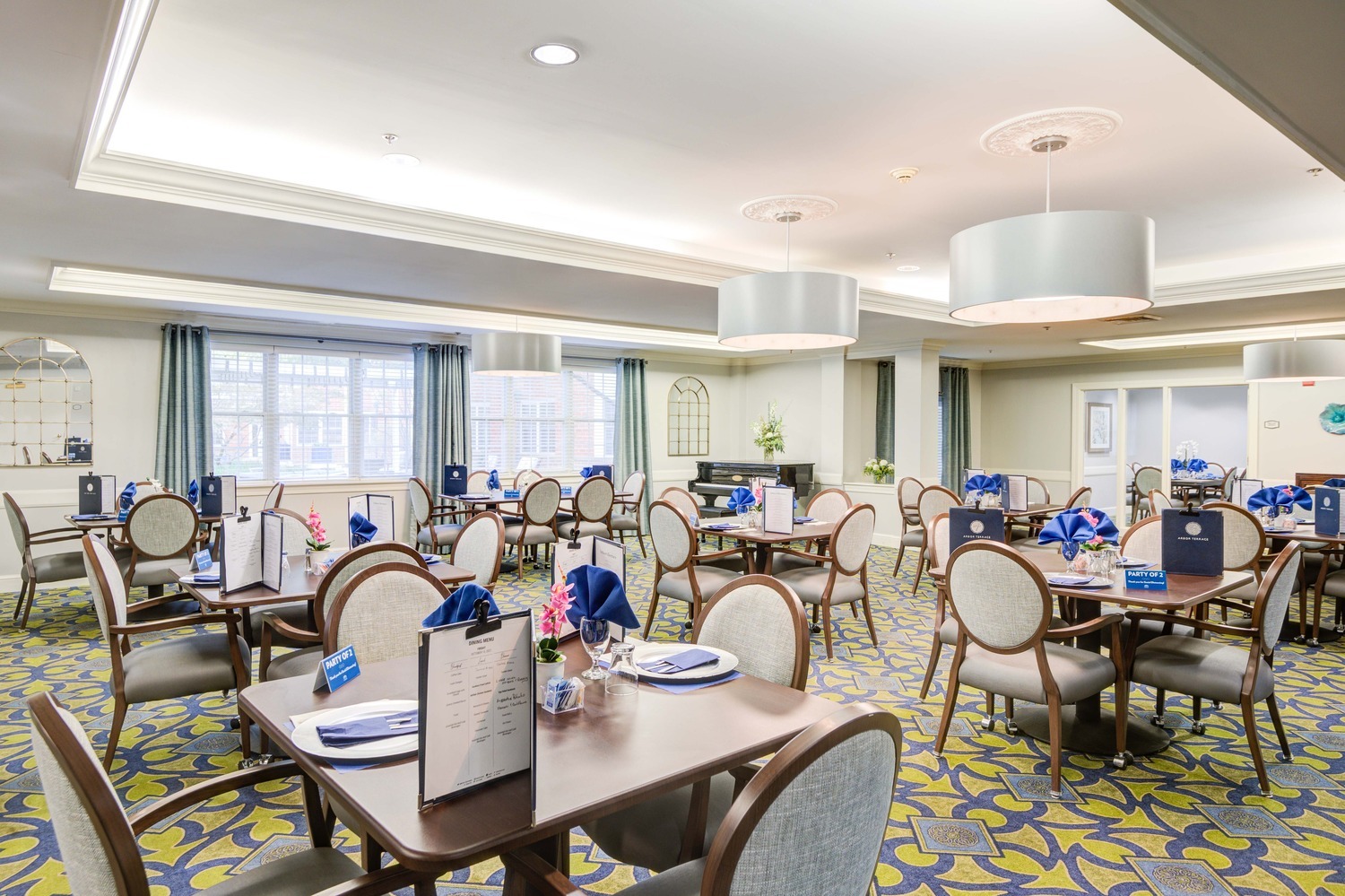 Spacious formal dining room with elegant table settings and patterned carpeting at Arbor Terrace, a top-rated senior living community with on-site dining in Lanham, MD.