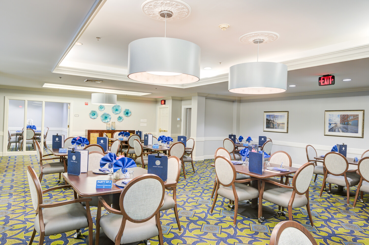 Another view of the cheerful dining room with vibrant carpet and neatly set tables at Arbor Terrace, a senior living community near Greenbelt Park in Lanham, MD.