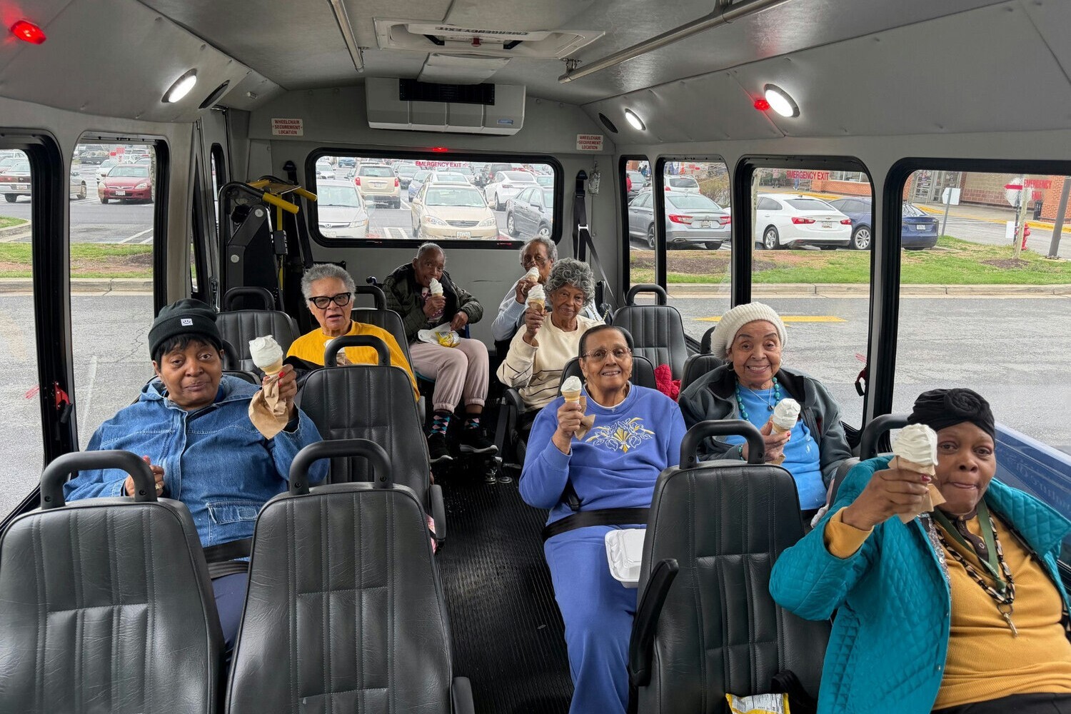 A group of residents smile and hold ice cream cones aboard a community outing bus at this active senior living community in Lanham, MD, enjoying one of many fun excursions.