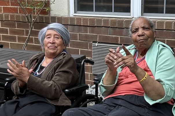 two senior ladies sitting outdoors and clapping
