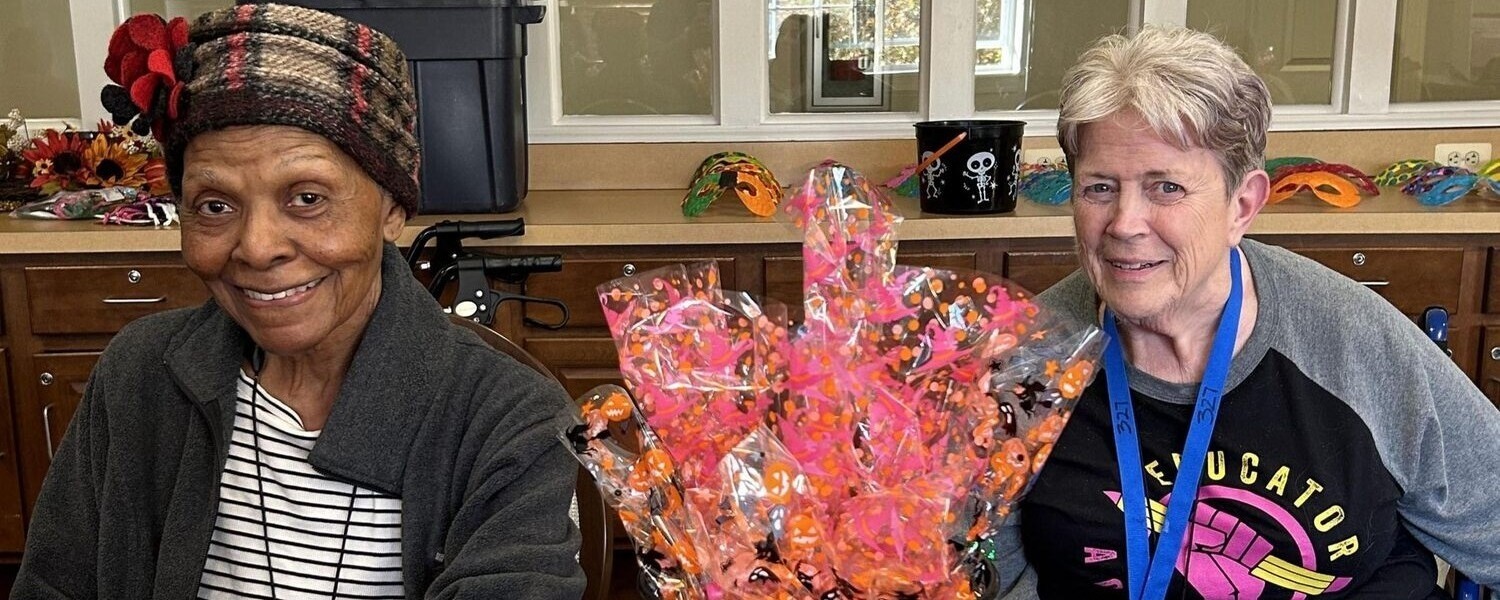 Two residents smile warmly while holding colorful wrapped gift baskets at a festive gathering at this senior living community in Lanham, MD, where social activities bring neighbors together year-round.