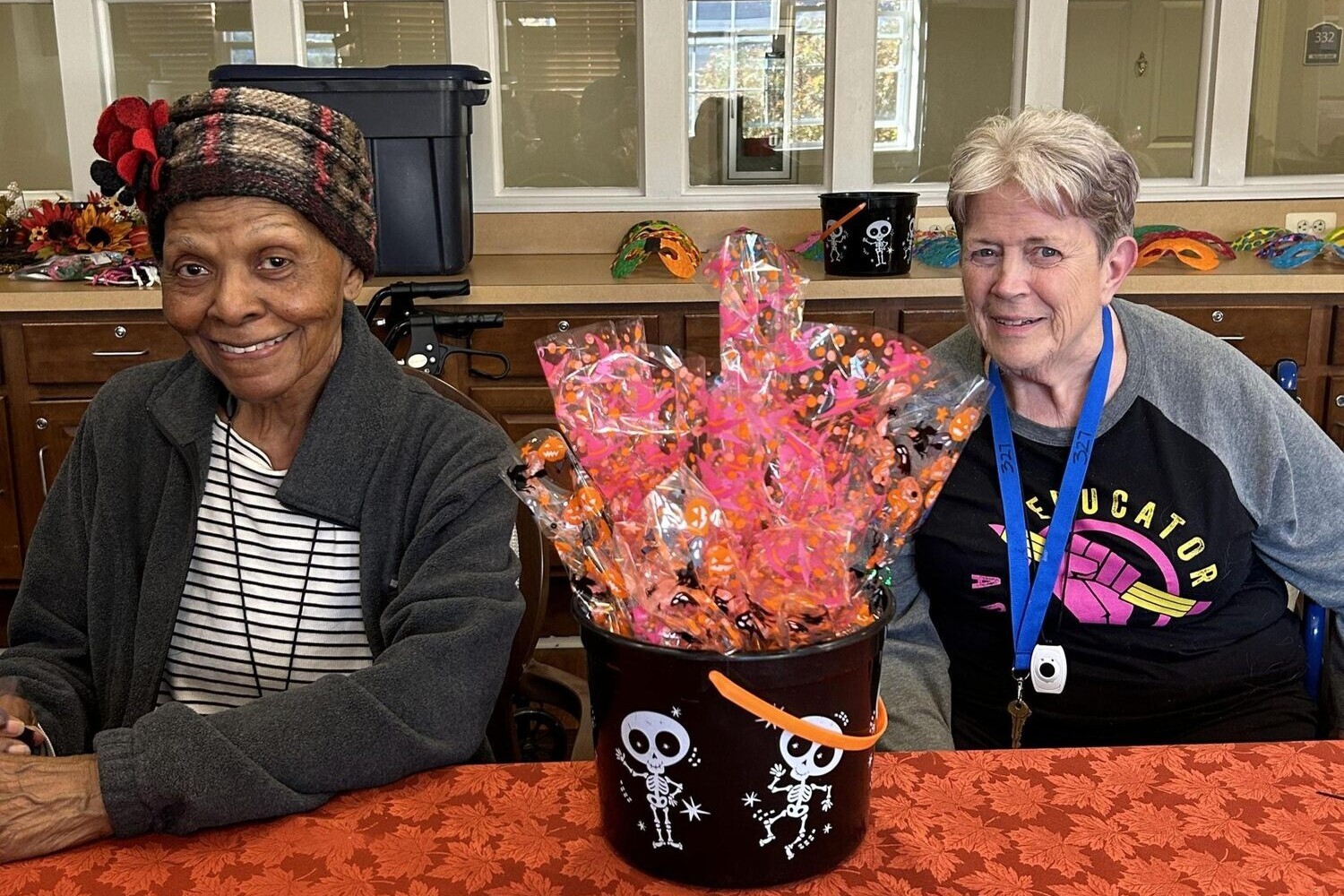 A resident and staff member smile together beside a festive Halloween gift basket at this senior living community in Lanham, MD, where seasonal social activities bring joy throughout the year.