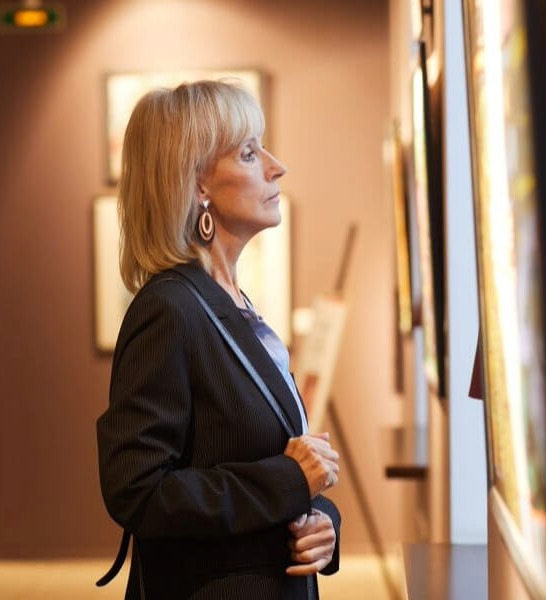 A woman quietly admires framed artwork displayed along a gallery wall, reflecting the cultured senior living in Sandy Springs, GA and Perimeter, GA.