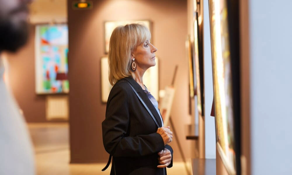 A person admiring artwork in a gallery, reflecting the vibrant cultural activities available to seniors near Arbor Terrace, an active senior living community in Lanham, MD near Greenbelt.
