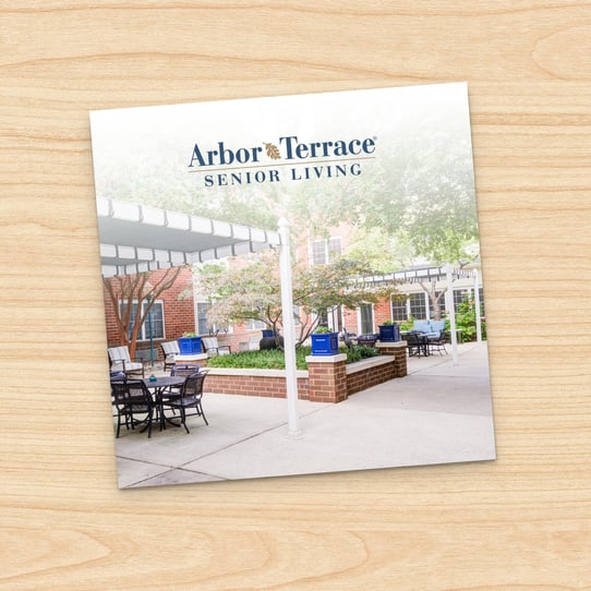 Square photo of Arbor Terrace Greenbelt outdoor courtyard patio with seating area and landscaped planter, displayed on a printed card against a wood-grain background