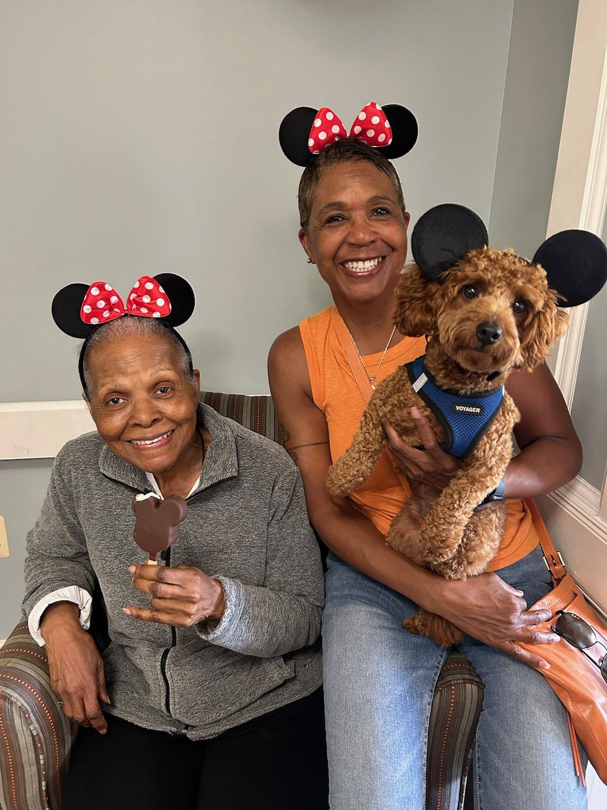 A resident and a family member sharing a joyful moment with an adorable dog, wearing festive ears at Arbor Terrace, a pet-friendly senior living community in Lanham, MD near Greenbelt.