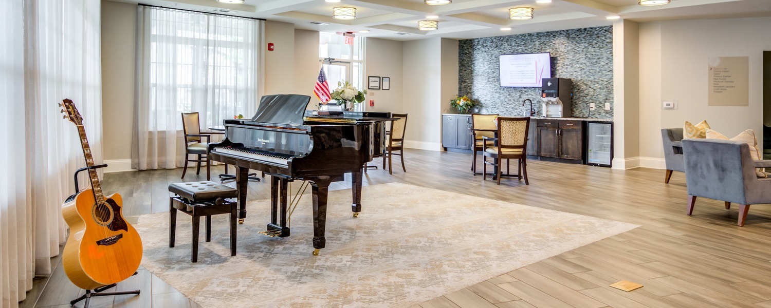 A bright and elegant common area featuring a grand piano and acoustic guitar at this independent living Dacula GA community, offering residents a welcoming space for music and relaxation.