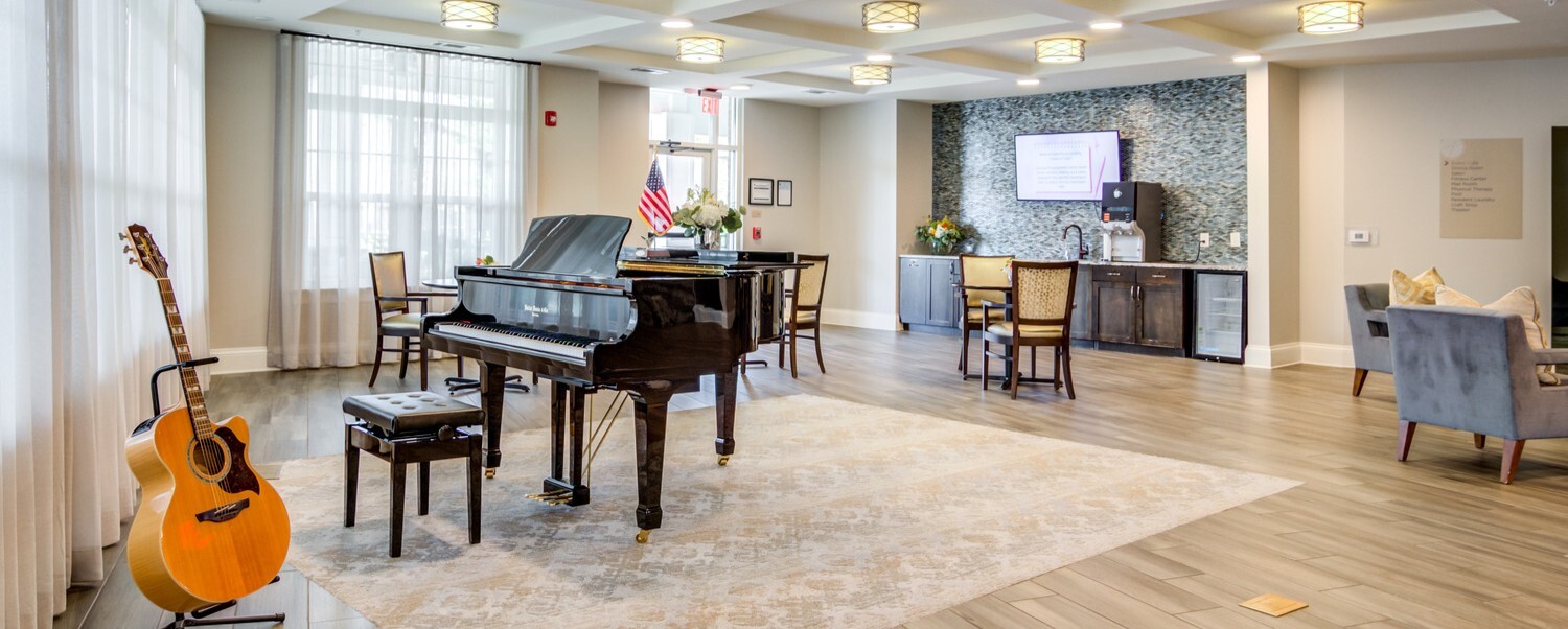 A spacious, elegantly appointed activity room at Arbor Terrace Hamilton Mill features a grand piano, acoustic guitars, and comfortable seating, offering residents in Dacula, GA a vibrant space for musical enrichment and social engagement.