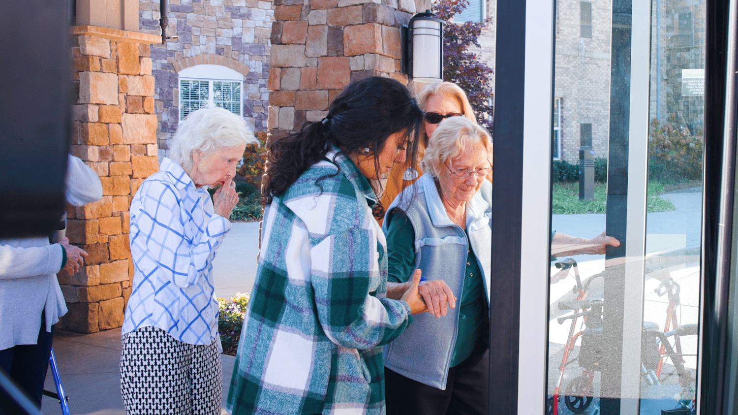 A group of seniors and a staff member head out together through the front entrance of this senior living community in Dacula, GA, enjoying an outing on a bright and sunny day.