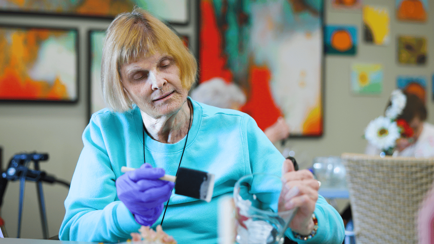 A senior focuses intently on a hands-on craft activity surrounded by colorful artwork at this senior living community near Hamilton Mill, GA, enjoying creative and engaging programming.