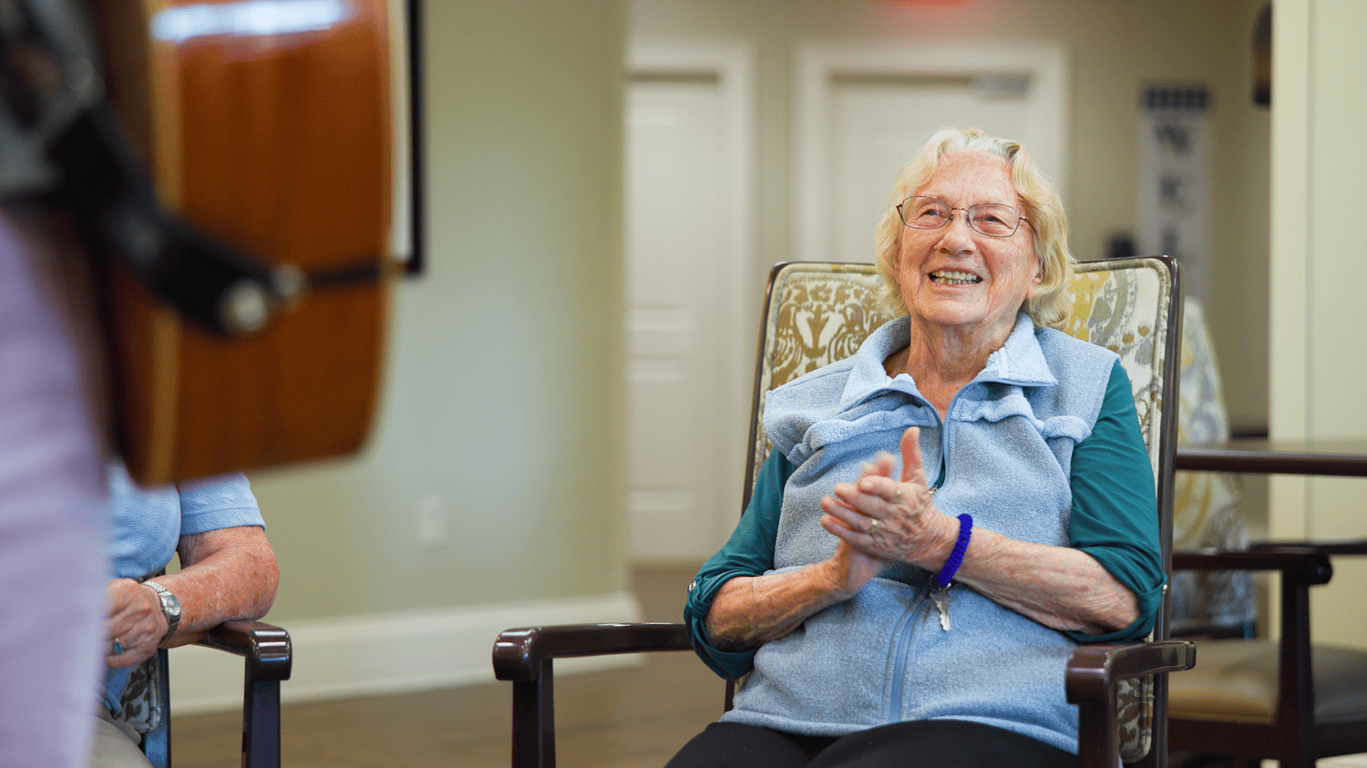 A senior claps and beams with joy while enjoying a live guitar performance at this senior living community in Dacula, GA, embracing the lively entertainment and activities offered.