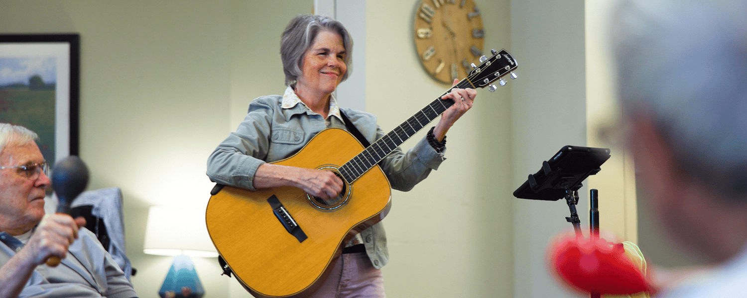 A guitarist performs a live music set while a senior resident participates with a handheld instrument, capturing the vibrant social and engagement-focused senior living experience in Dacula GA.