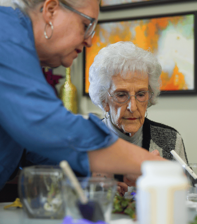 A staff member attends to a senior resident during a hands-on activity, reflecting the compassionate, person-centered memory care provided at this Dacula GA community.