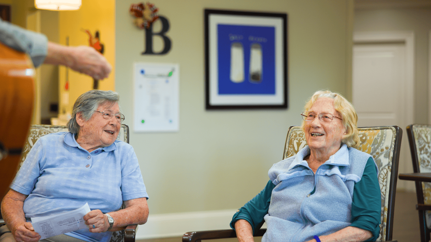 Two seniors share a joyful laugh while relaxing together in a cozy common area at this senior living community in Dacula, GA, enjoying warm company and a welcoming atmosphere.
