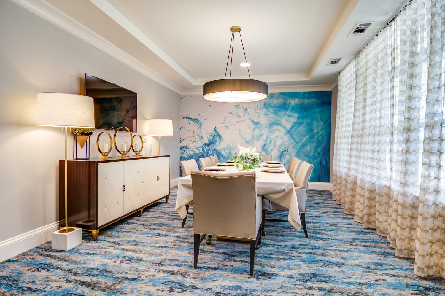 An elegantly appointed private dining room with a bold blue accent wall, soft carpeting, and warm pendant lighting at this senior living community near Hamilton Mill, GA.